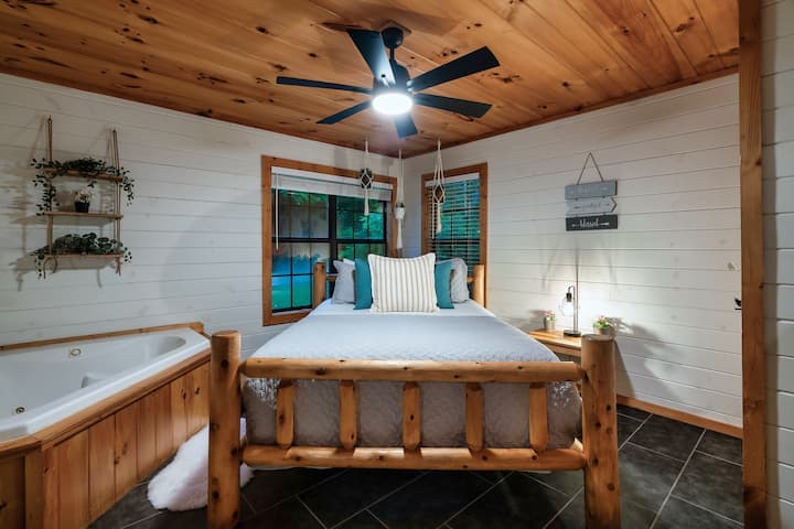 Rustic cabin suite: log bed, corner windows, and in-room jetted tub.