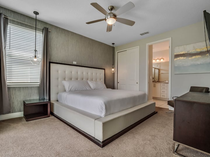 - Модерна брачна спална соба со бела тапацирана табла  
- Пристап до сопствена бања и удобност на вентилаторот на таванот  
- Стилски дизајн со висечки светилки и ѕидна уметност