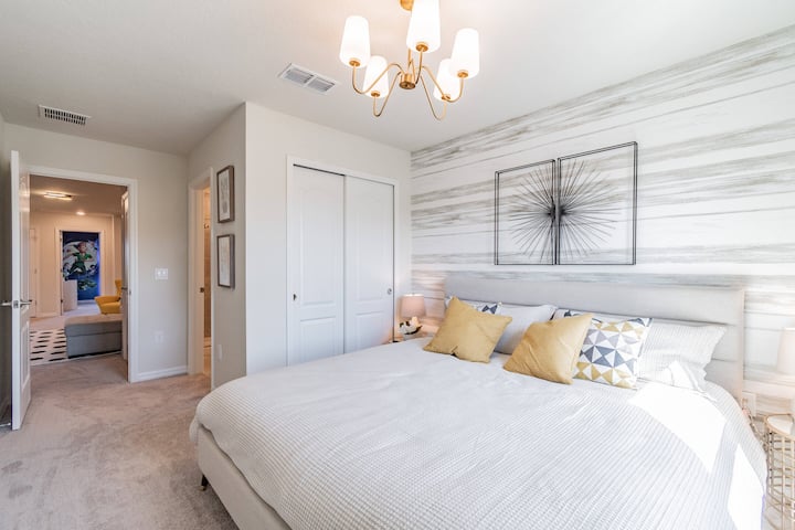 ادخل إلى غرفة نوم هادئة تتميز بسرير فخم بحجم كينج مزين بوسائد صفراء ناعمة. تضفي الثريا الأنيقة توهجًا دافئًا، مما يعزز الأجواء الهادئة التي يكملها الجدار المخطط الرقيق.