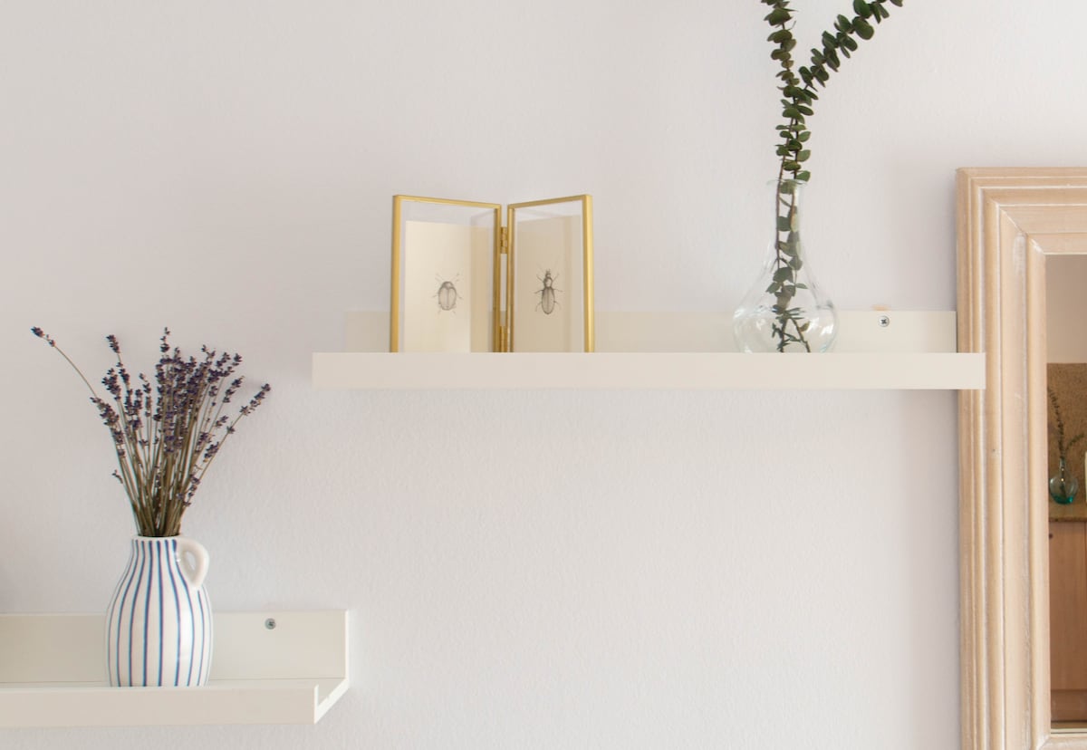 A narrow shelf displays a decorative vase containing greenery and dried lavender. A small, framed display featuring two insect specimens is positioned next to the vase, adding a unique visual element to the light-colored wall.