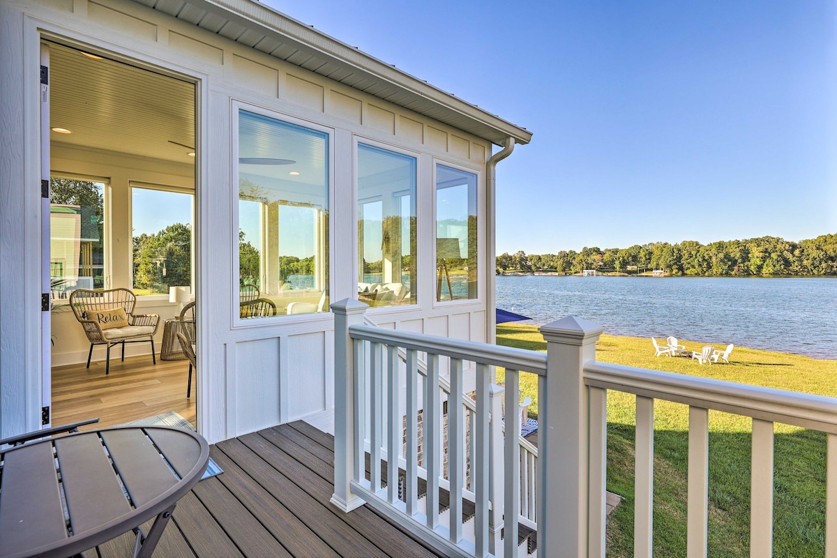 A view from a private balcony showcases a serene lake and lush greenery. The space features modern glass windows allowing plenty of natural light. Comfortable seating is visible inside, creating a connection between indoor and outdoor areas.