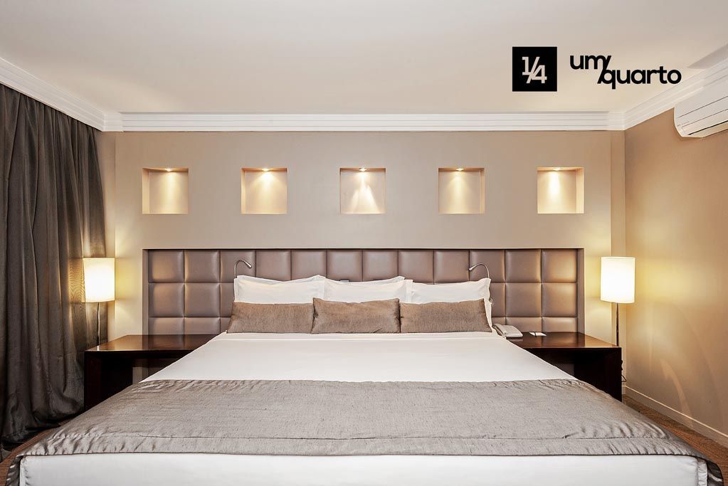 A spacious sleeping area features a large bed with a brown upholstered headboard, complemented by decorative wall niches illuminated softly. The room contains two bedside lamps and dark curtains, adding to the modern aesthetic.