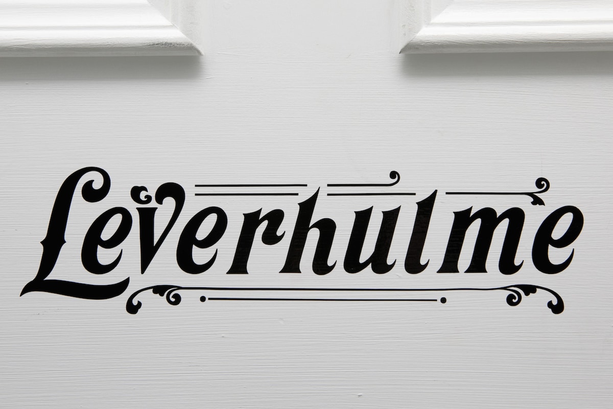 The name 'Leverhulme' is elegantly displayed in a decorative black font, affixed to a white door. The design features ornate detailing that adds a sense of character to the entrance.