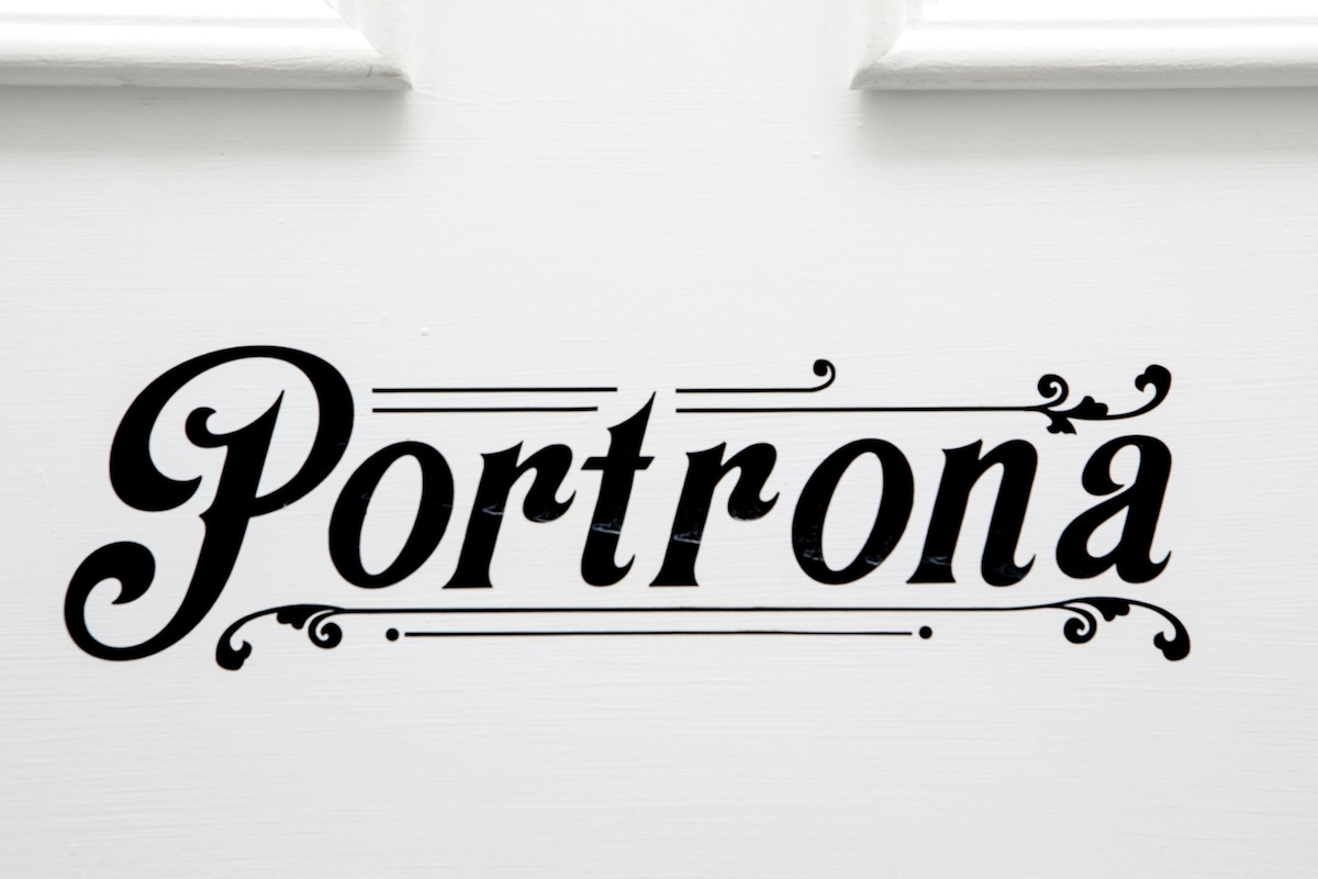 The sign displaying the name 'Portrona' is styled in an elegant black font against a white background. The design features ornate detailing that adds a refined touch to the entrance.