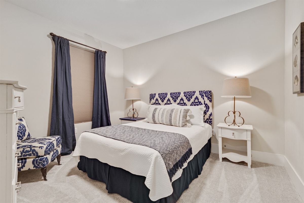 חדר האורחים המאובזר היטב כולל מיטת קווין סייז עם ראש מיטה דקורטיבי, מצעים לבנים ומצוחצחים, שידות לילה תואמות עם מנורות וריצוף אריחים לתחזוקה קלה.