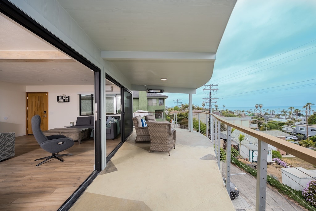 A spacious private balcony features comfortable outdoor seating and stunning views of the ocean and surrounding landscape. Large sliding glass doors invite natural light into the living area, enhancing the sense of openness. The modern architecture of the building is evident in the clean lines and design.