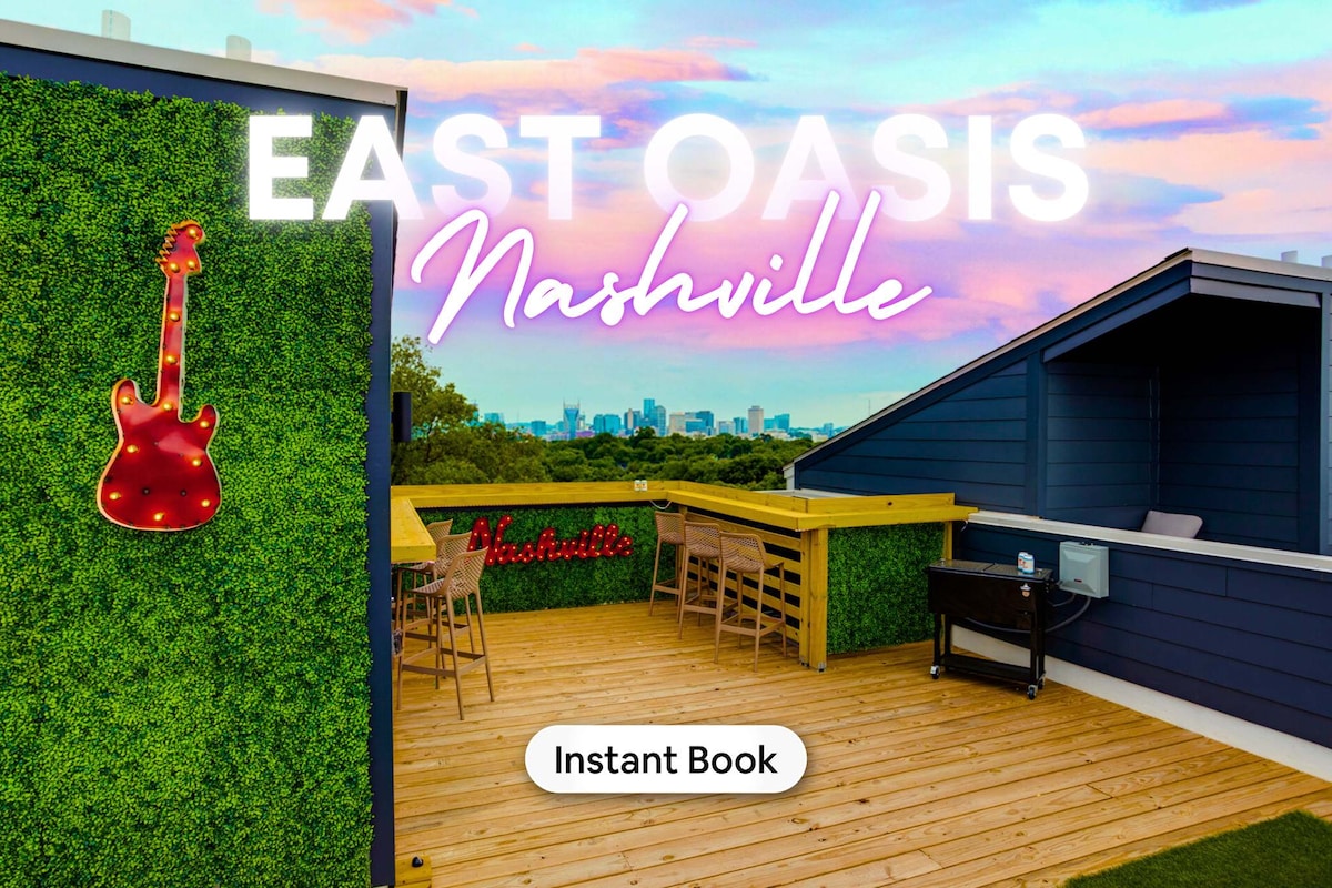 A spacious rooftop terrace features wood decking and green wall accents. A decorative guitar with lights adds character, while a wooden bar counter and multiple stools provide seating. The skyline of Nashville is visible in the background against a colorful twilight sky.