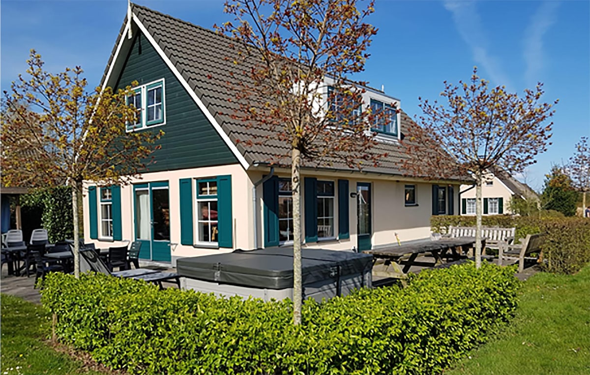 A spacious vacation home is depicted, featuring a combination of dark green and light-colored siding. Large windows are arranged symmetrically across the façade, allowing natural light to illuminate the interior. Surrounding greenery and outdoor seating areas are visible, suggesting a comfortable outdoor space.