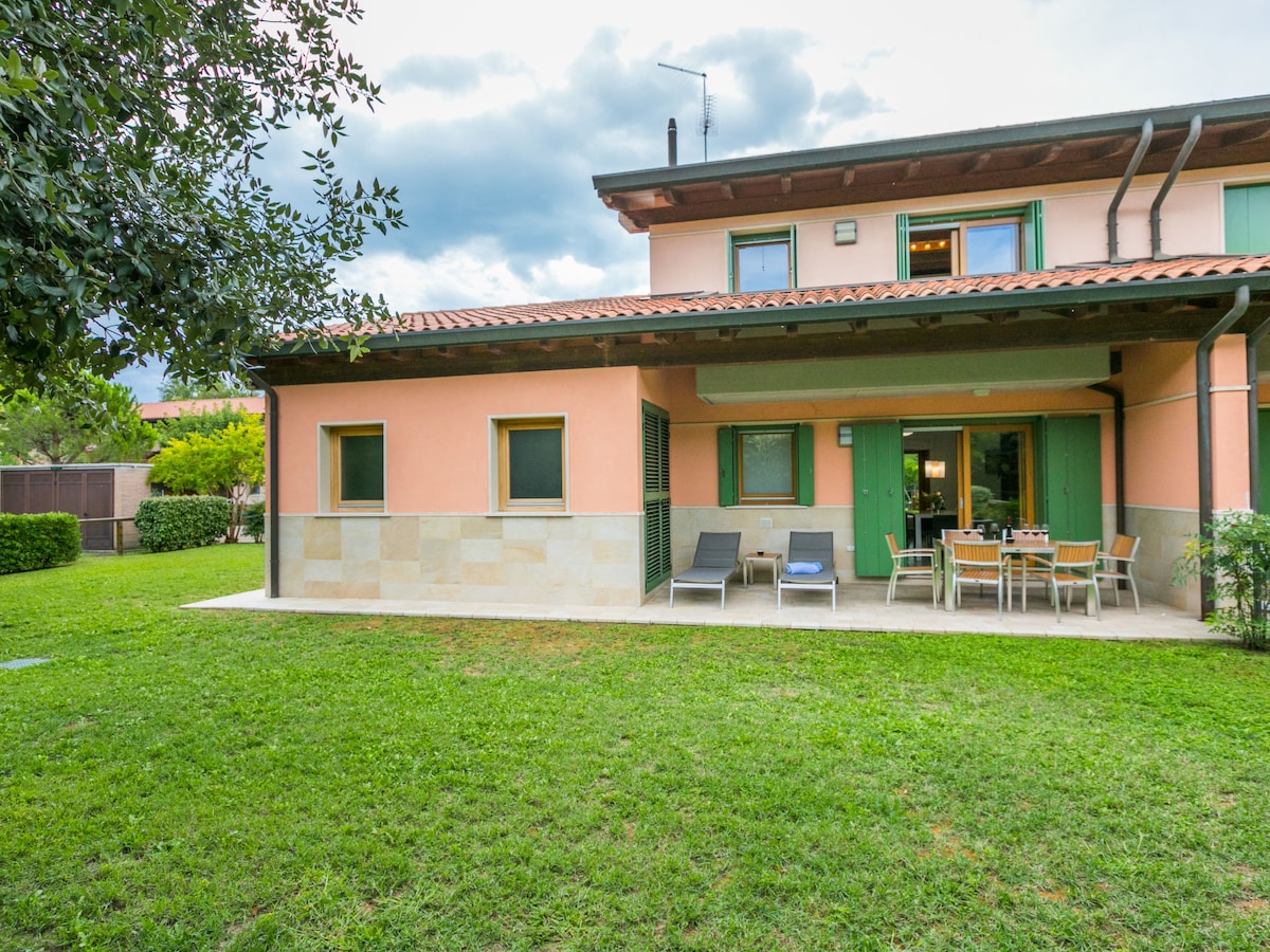 A semi-detached house features a spacious outdoor area with a well-maintained lawn. Patio furniture, including loungers and a dining table, is arranged on the terrace, providing ample space for relaxation and outdoor dining. Large windows invite natural light into the interior.
