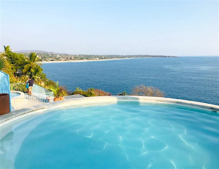 A private dipping pool is seen with a clear blue surface, framed by a picturesque landscape. The expansive view showcases the Pacific Ocean and coastline in the distance, with lush greenery surrounding the area, offering a serene and refreshing escape.