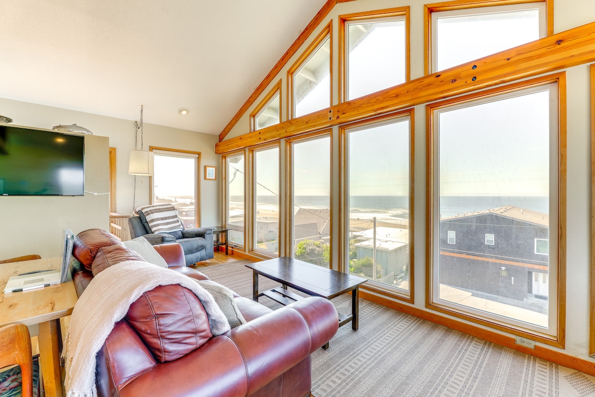 A spacious living area is highlighted by large windows offering sweeping ocean views. Natural light fills the room, which features a comfortable leather sofa and a recliner. A coffee table sits centrally, and a flat-screen TV is mounted on the wall.
