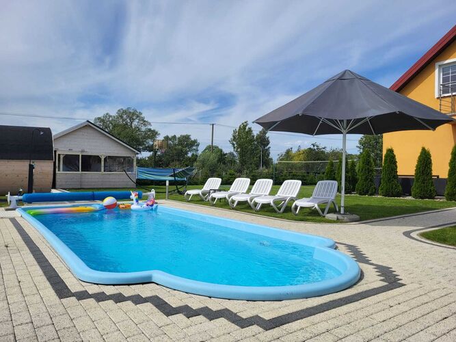 A spacious pool area features a vibrant blue swimming pool surrounded by lounge chairs and shaded by a large umbrella. Colorful inflatable toys float in the water, and a cozy gazebo is visible in the background, enhancing the relaxing outdoor setting.