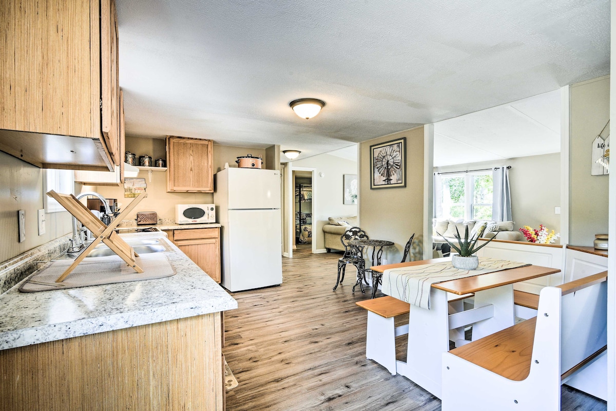 An open kitchen and dining area features a spacious table with bench seating. Light wood cabinetry complements the modern appliances, including a white refrigerator and stove. A window allows natural light to brighten the space, enhancing the inviting ambiance of the home.