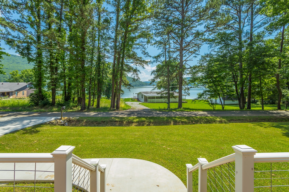 The view from the front deck reveals lush green trees surrounding a clear view of Nick-a-Jack Lake. A grassy area leads to the water, which is framed by the natural landscape, creating a serene atmosphere perfect for relaxation.