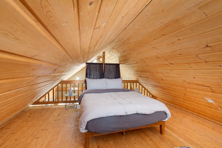 Уютната спалня на тавана ви обгръща с топло дърво, създавайки интимно уединение, където свежото спално бельо очаква спокойната ви нощ.