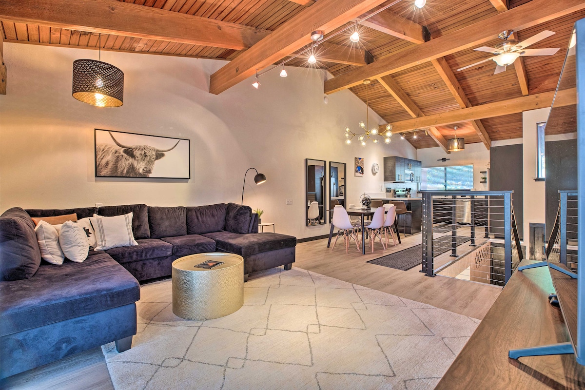 A spacious living area is highlighted by high wood beam ceilings and natural light. A large sectional sofa, accented by decorative pillows, is complemented by a round coffee table. A dining area with modern chairs and a view of the kitchen adds to the inviting ambiance.