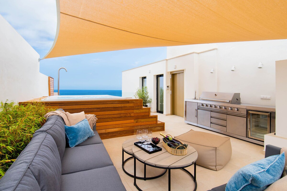 A spacious terrace features a sleek outdoor seating area, accompanied by a coffee table and a plush ottoman. A BBQ grill is positioned nearby, while a private pool is visible against the backdrop of a sea view. A sunshade extends overhead for comfort.