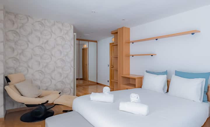 Una elegante habitación doble en Sports Villa Banyoles, con una cómoda cama, una acogedora tumbona y modernos muebles de madera.