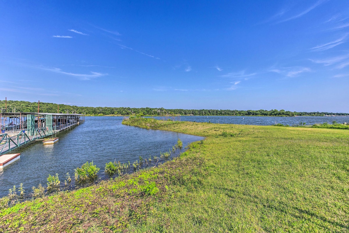 A scenic view of Lake Texoma is displayed, showcasing a mix of serene water and green grass. The shoreline appears gentle, with patches of vegetation along the water's edge, set against a clear blue sky.