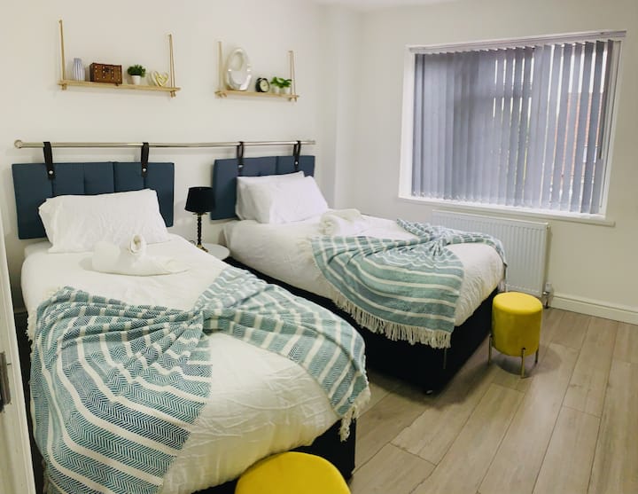 Светла и приветлива спалня с 2 единични легла, смарт телевизор и голям прозорец за естествена светлина и гледка. Украсено с изкуствени цветя, стенен часовник и маса за чекмеджета за допълнително съхранение и удобство.