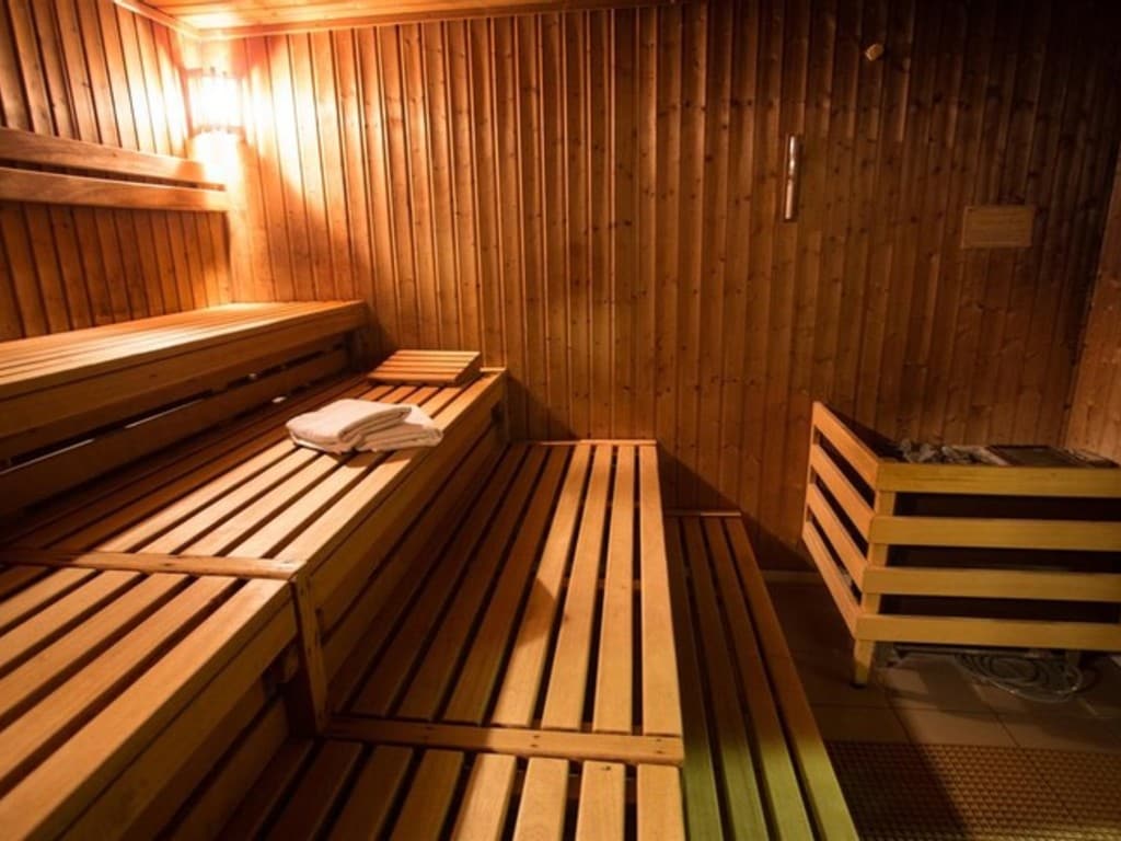 A wooden sauna environment features tiered seating made of slatted wood. Towels are neatly placed on the upper benches. The walls are lined with wooden panels, and soft lighting enhances the warm atmosphere, inviting guests to unwind and relax.