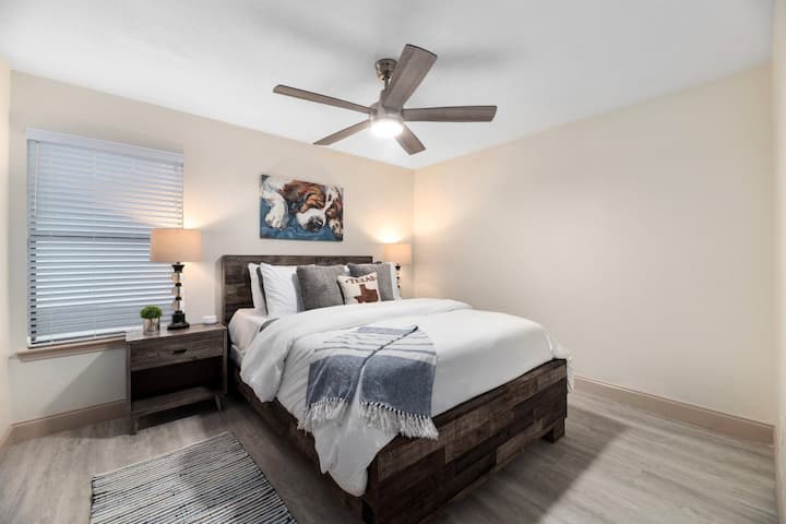 Dormitorio cálido y acogedor con marco de cama de madera rústica, sábanas acogedoras en capas, ventilador de techo y tonos neutros relajantes.