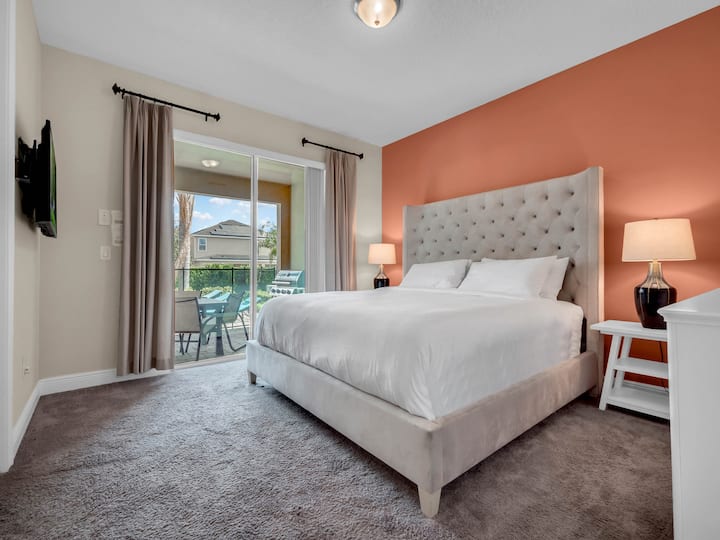 - Bedroom with coral accent wall and king bed opening to patio views  
- Bright space with sliding doors for fresh air and natural light  
- Perfect retreat for couples during Orlando family vacation stays