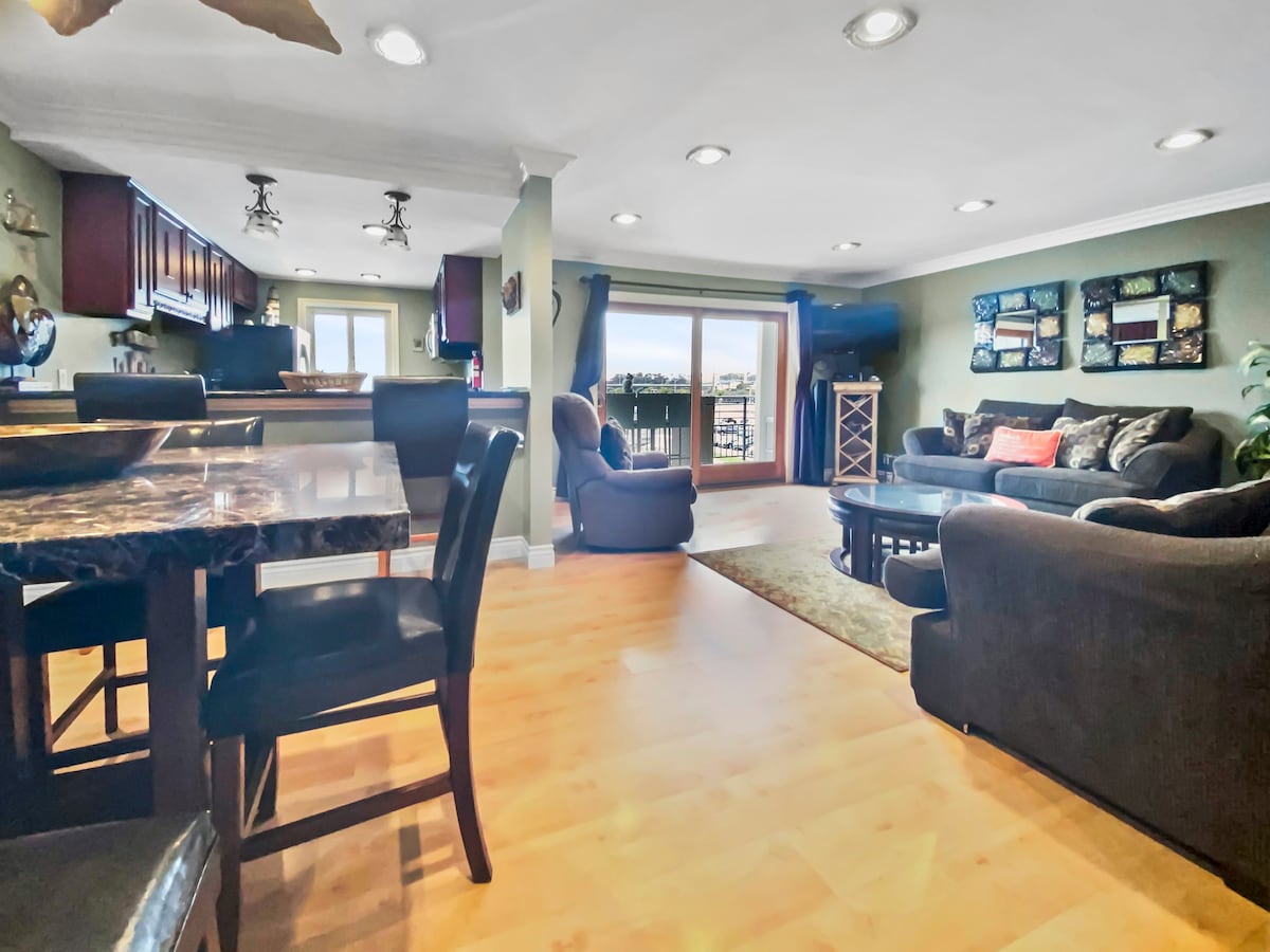 A spacious living and dining area features a dark wood dining table and black chairs. A cozy seating arrangement includes a dark couch and armchairs, with natural light streaming in through sliding glass doors that open to a private patio.