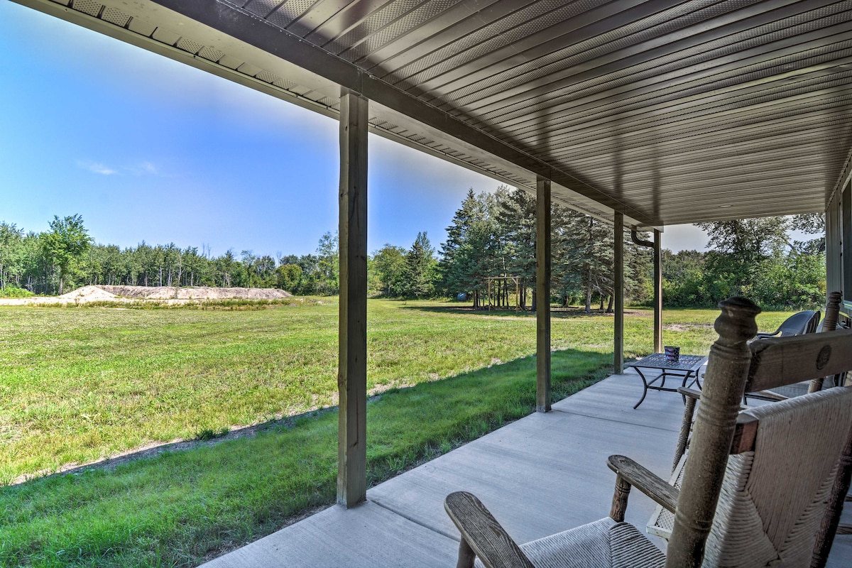 A spacious covered porch is showcased, featuring comfortable rocking chairs. Beyond the porch, a large grassy area stretches towards a tree line, providing a serene view of the surrounding nature.