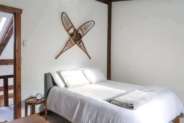 Chumba cha kulala cha viatu vya theluji cha ghorofa ya juu kina kitanda cha kifahari kilicho na matandiko ya mashuka ya kifahari na kina uwakilishi wa sanaa wa burudani ya majira ya baridi katika Catskills.