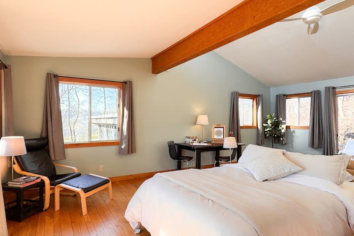 Sunny bedroom with desk, lounge chair, and wooded views