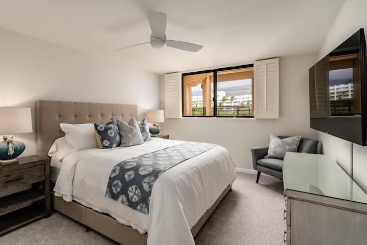 Moderná spálňa s všívanou posteľou, televízorom na stene a oknom.