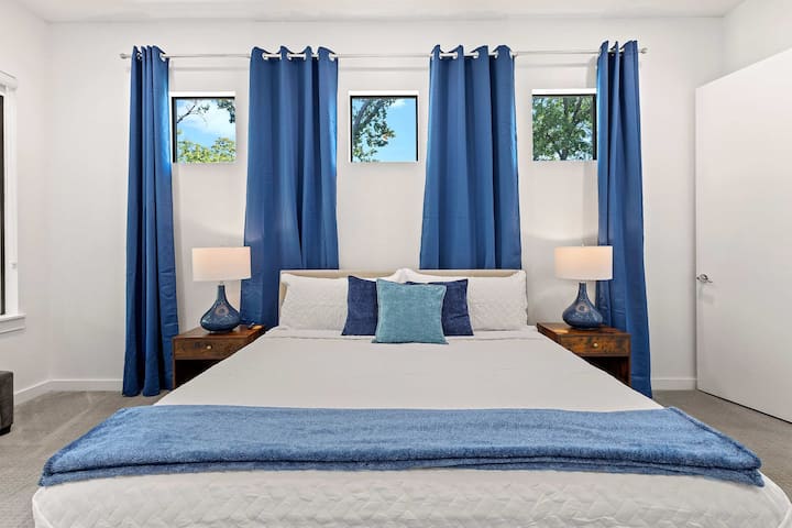 Spacious primary bedroom featuring rich blue drapes, cozy lighting, and a calming modern vibe.