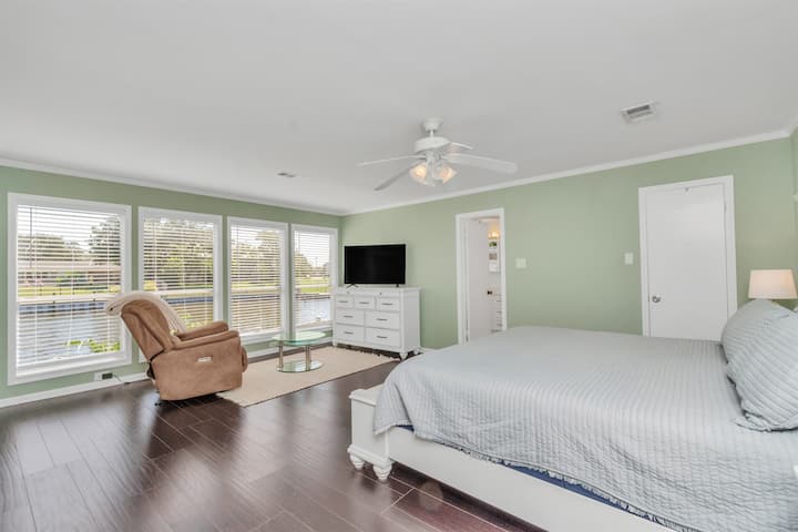 Vistas imponentes del lago desde el dormitorio principal con acceso de puerta abierta a la plataforma. ¡Disfruta de una película en la televisión de pantalla grande o simplemente relájate en el sillón con un libro!