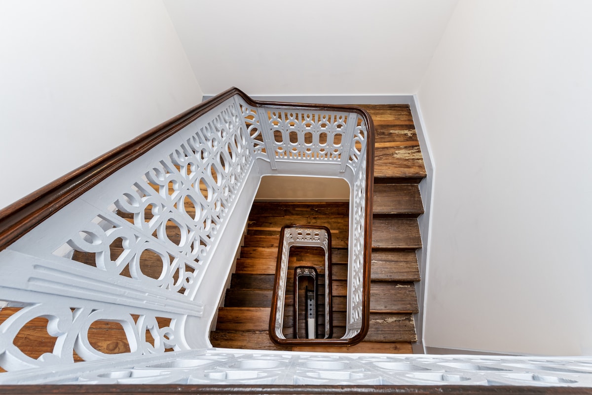 A spiral staircase is featured, showcasing ornate wooden steps and a decorative metal railing. The light wood of the stairs contrasts with the white railing, creating a bright and airy feel. The staircase leads up to the second floor, framed by smooth walls.