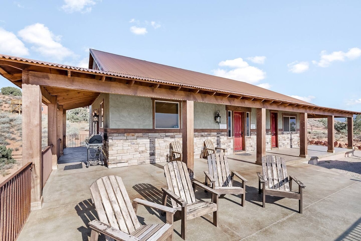 A welcoming outdoor patio features several wooden lounge chairs arranged for relaxation. The structure is enhanced by a sturdy roof and stone accents, with large windows on the sides allowing for natural light. Scenic views of the surrounding landscape are visible in the background.