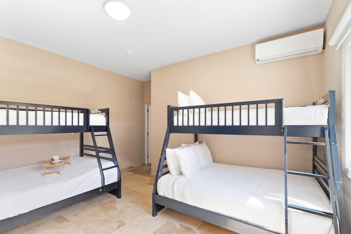 חדר שינה אופנתי בווילה בנורד ארובה - מיטות בונקר נוחות - חדר מעוצב באלגנטיות - קירות צבועים יפהפיים עם קישוט - מנורות שולחן מלכותיות - מצעים נקיים ומסודרים - חלונות גדולים עם נוף יפהפה - טלוויזיה ונטפליקס זמינים