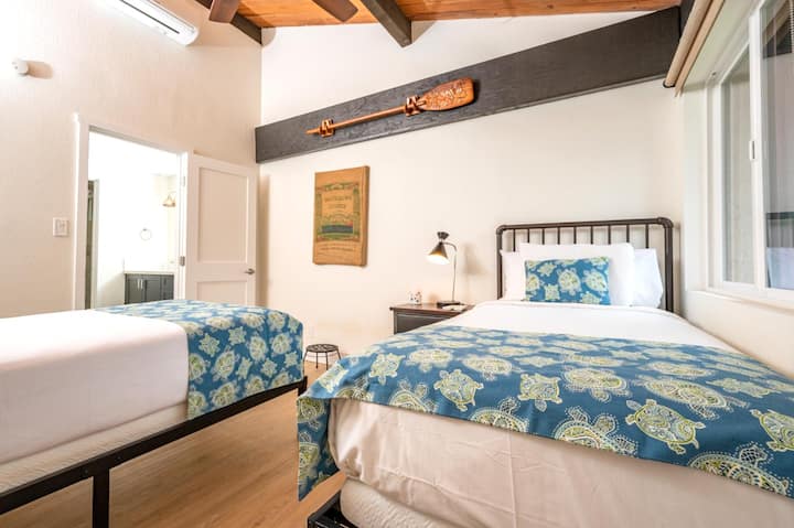 ห้องพักที่มีสไตล์พร้อมเตียงเดี่ยว 2 เตียง เพดานโค้ง ลายพิมพ์เขตร้อน และวิวสวนเขียวชอุ่มที่สดใส