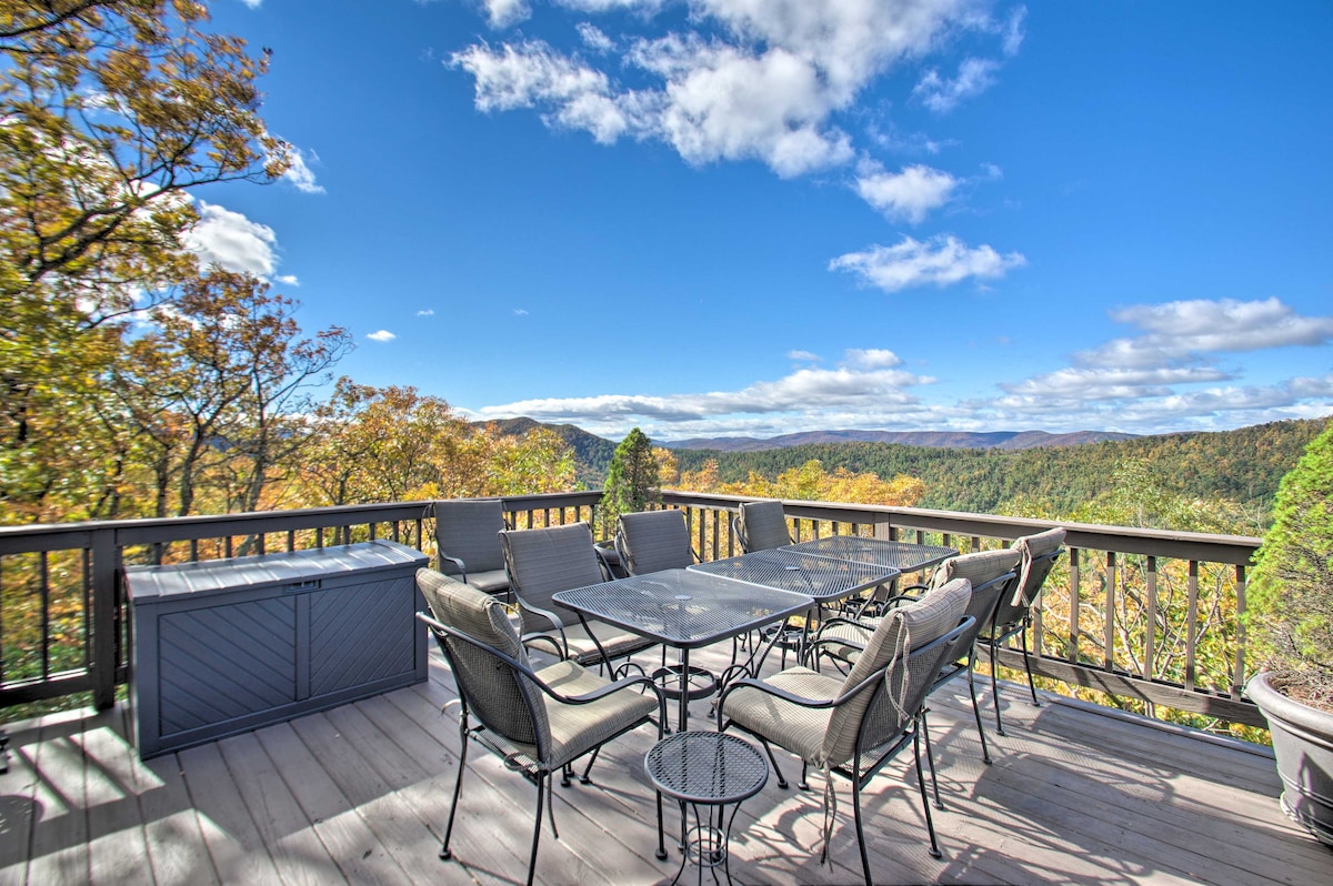 A spacious multi-level deck features a large table surrounded by six dining chairs, with a cozy seating area nearby. The area offers panoramic mountain views, highlighted by vibrant autumn foliage under a clear blue sky.
