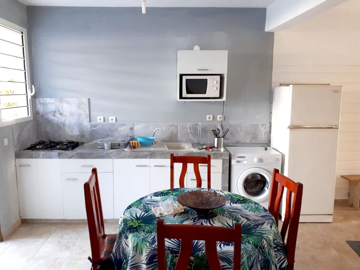 A fully equipped kitchen features modern appliances, including a refrigerator, microwave, and stove. A round dining table with chairs is positioned in the space, complemented by a decorative tablecloth. A washing machine is also included, providing convenience for guests.