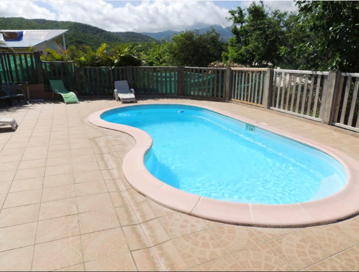 A private pool with a rounded shape is surrounded by a tiled patio. Lush greenery and distant hills provide a natural backdrop, enhancing the tranquil space. Lounge chairs are positioned nearby, offering options for relaxation in the sun.