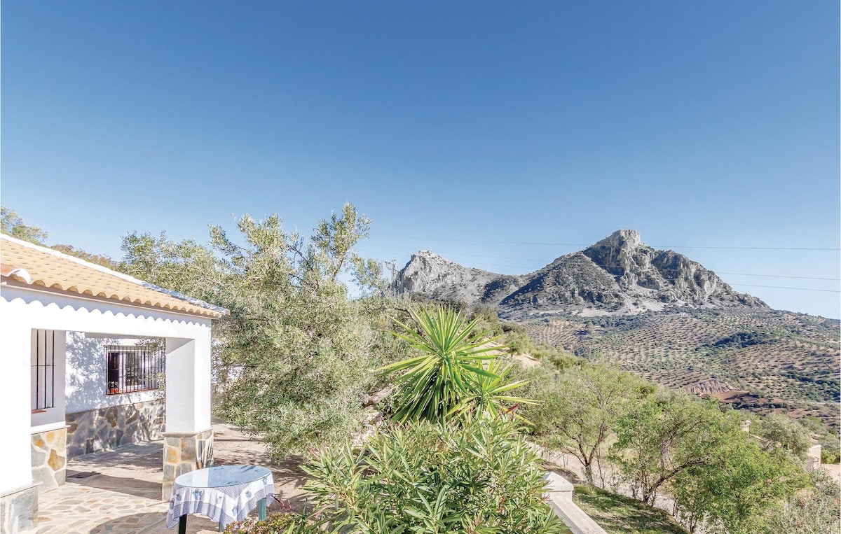 A view of the vacation home reveals a charming exterior accompanied by a covered porch. Lush greenery surrounds the property, contrasting with the rugged mountain backdrop under a clear blue sky.