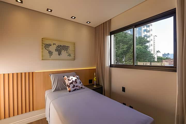 Quarto de solteiro moderno e acolhedor, ideal para relaxar e produzir com conforto. Conta com ar-condicionado, TV, armário e espaço para estudo ou home office. Cortinas blackout garantem privacidade e noites de descanso perfeitas.
