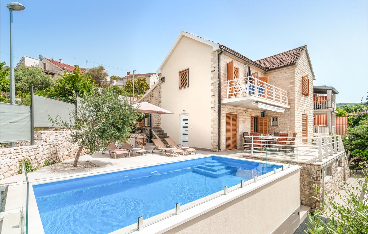 A modern vacation home is presented with a private outdoor pool and spacious terrace. Sun loungers surround the pool, and shaded areas are provided by umbrellas. The two-story structure features a mix of stone and modern materials, enhancing the outdoor living experience.