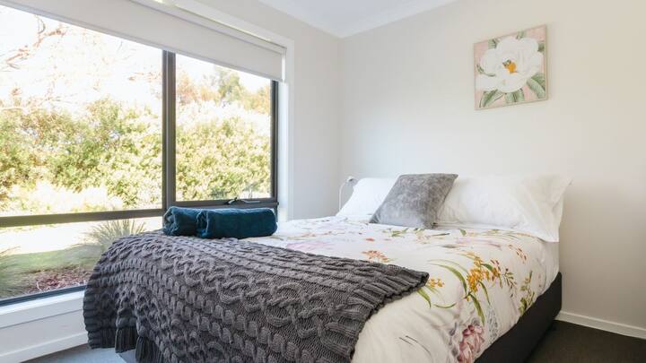 Ground level Queen Room na may cot na nakaposisyon sa kanan ng higaan sa kahabaan ng pader.