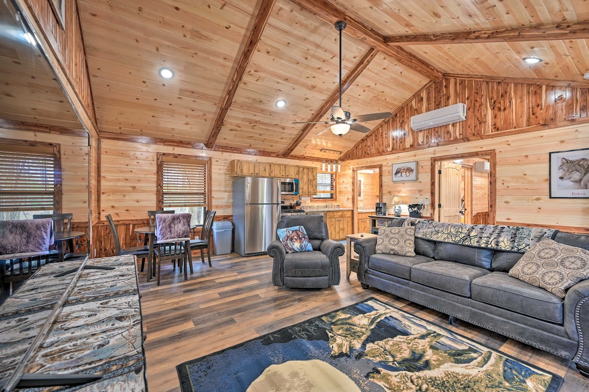 A spacious living area features wood-paneled walls and ceiling, enhancing a rustic charm. A comfortable sofa, textured cushions, and a patterned area rug are positioned around a coffee table. A dining space with four chairs is visible, alongside modern kitchen appliances.