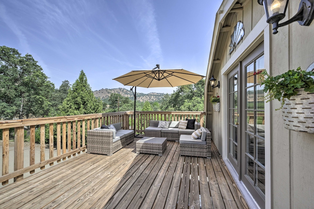 A private balcony features comfortable outdoor seating arrangements, including a sectional sofa and a coffee table. An umbrella provides shade, while the wooden deck offers a clear view of the surrounding greenery and hills, creating a serene outdoor space.