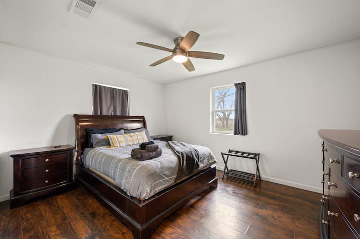 Rest peacefully in your comfortable bedroom featuring dark wood furnishings, ceiling fan, and natural light streaming through the window.   (no TV)