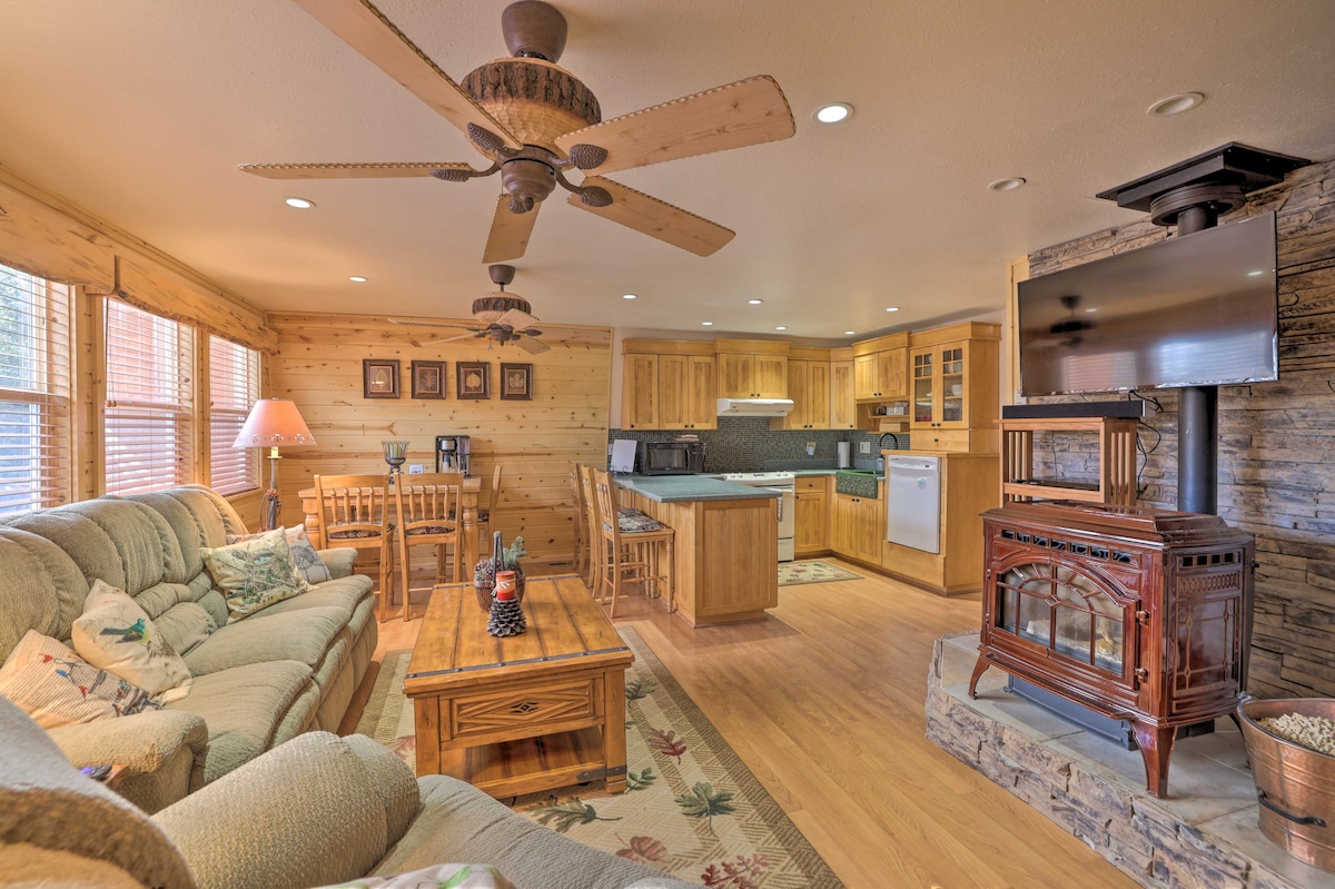 The living area features a comfortable sofa and a wooden coffee table, complemented by a warm electric fireplace. A Smart TV is mounted on a stone wall opposite the seating. Light pours in through multiple windows adorned with wooden blinds, emphasizing the cabin's welcoming design.