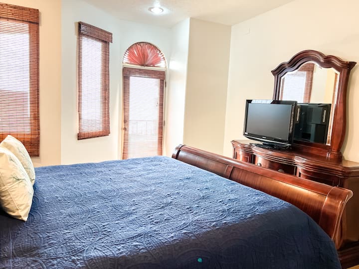 Примарна спална соба со брачен кревет, вентилатор на таванот, сопствена бања, ноќни шкафчиња и телевизор.